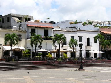 Blick auf die kolonialen Gebäude in Santo Domingo, umgeben von Palmen und einem einladenden Platz mit Tischen.