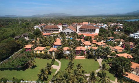 Eine Luftaufnahme des Radisson Blu Resorts in Goa, umgeben von üppigem Grün und bunten Gebäuden mit roten Dächern.