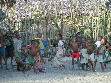 Eine Gruppe fröhlicher Kinder spielt am Strand, einige lachen und posieren, während andere in Bewegung sind.
