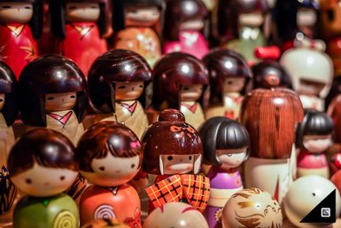 Eine Vielzahl von Kokeshi-Puppen in verschiedenen Farben und Designs, die in einem lebhaften, traditionellen japanischen Stil präsentiert werden.