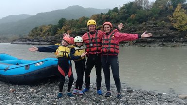 Eine fröhliche Familie posiert am Ufer eines Flusses, bereit für ein aufregendes Rafting-Abenteuer in der Natur.