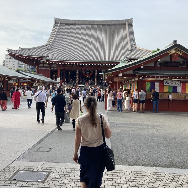 Eine Menschenmenge besucht den Senso-ji Tempel, während eine Frau in einem weißen Oberteil in Richtung des Tempels geht.