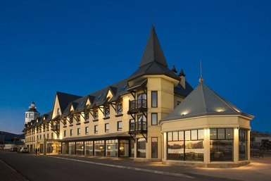 Ein elegantes Hotel mit spitzen Türmen und großen Fenstern, das in der Dämmerung beleuchtet ist.