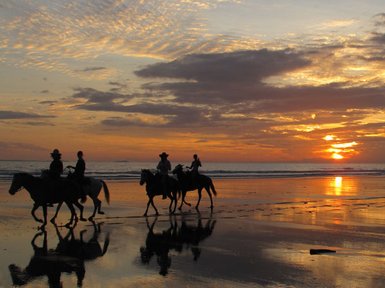 Reiter auf dem Strand genießen den Sonnenuntergang, während ihre Schatten auf dem nassen Sand reflektiert werden.