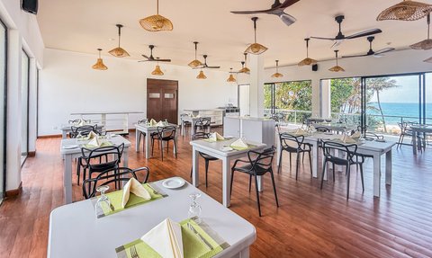 Ein helles, modernes Restaurant mit vielen Tischen und Stühlen, umgeben von großen Fenstern mit Blick auf das Meer.