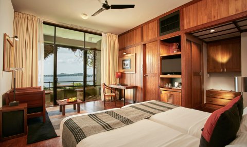 Ein stilvolles Zimmer mit zwei Betten, Holzverkleidung und Blick auf einen ruhigen See durch große Fenster.