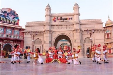 Eine Gruppe von Tänzern in traditioneller Kleidung führt eine lebhafte Darbietung vor dem Eingang zu Bollywood Parks Dubai auf.