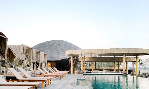 Elegante Liegestühle mit sanften Vorhängen säumen den Poolbereich eines stilvollen Resorts am Meer, umgeben von natürlicher Schönheit.