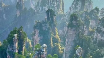 Majestätische, hoch aufragende Felsen sind von üppigem Grün umgeben, während der Nebel die Landschaft mystisch erscheinen lässt.