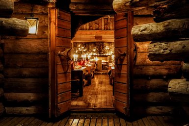 Die offene Holztür eines rustikalen Restaurants mit warmem Licht und einem einladenden Ambiente, das zum Verweilen einlädt.