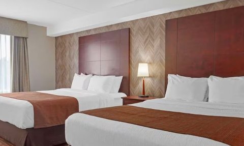 Ein modernes Hotelzimmer mit zwei bequemen Betten, eleganten Holzpaneelen und einem großen Fenster, das Tageslicht hereinlässt.