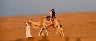 Beduin führt Kamele mit Mutter und Tochter durch die Wüste – Oman Familienreise