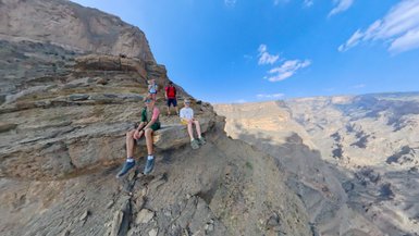 Familie macht eine Pause auf einem Felsen und blickt über die beeindruckende Schlucht des Jebel Shams – Oman mit Kindern