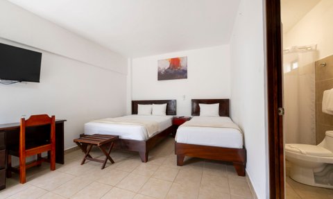 Ein helles Zimmer mit zwei Einzelbetten, einem Schreibtisch und einem Fernseher an der Wand, ideal für einen entspannten Aufenthalt.