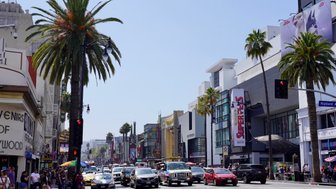 Eine belebte Straße in Hollywood mit Palmen, Autos und Menschen, die die Geschäfte und Sehenswürdigkeiten erkunden.