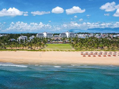 Ein atemberaubender Blick auf den Hoi An Strand mit einem luxuriösen Resort im Hintergrund und Palmen, die sanft im Wind wiegen.