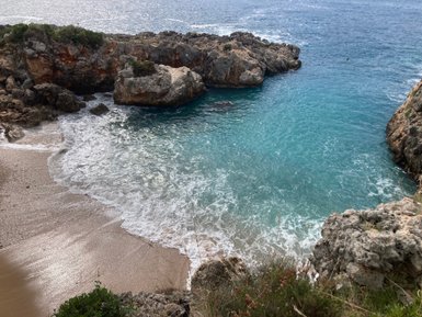 Eine ruhige Bucht mit klarem, türkisfarbenem Wasser, umgeben von felsigen Klippen und sanften Wellen am Strand.