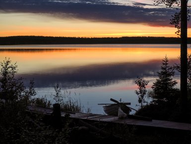 Ein ruhiger Abend am See, wo sanfte Wellen das orangefarbene Licht des Sonnenuntergangs reflektieren.