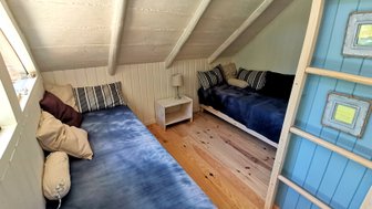 Der gemütliche Raum verfügt über zwei Einzelbetten mit blauen Bettdecken und Kissen, umgeben von hellen Wänden und Holzfußboden.