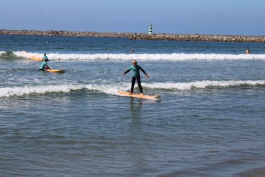 Ein junger Surfer balanciert geschickt auf seinem Surfbrett in den sanften Wellen des Strandes.