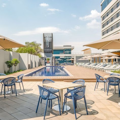 Ein eleganter Poolbereich im Radisson Hotel Johannesburg, umgeben von Sonnenschirmen und modernen Liegen.