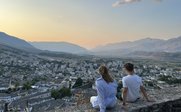 Ein Paar sitzt auf einer Mauer und blickt auf die Stadt, während die Sonne hinter den Bergen untergeht.