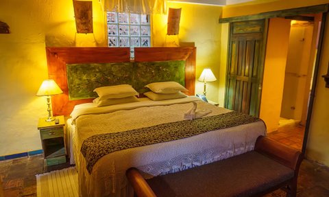 Ein gemütliches Schlafzimmer mit einem großen Bett, sanften gelben Wänden und warmem Licht von einer Tischlampe.