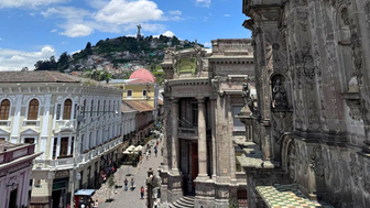 Ein lebhaftes Stadtbild mit historischen Gebäuden, Menschen auf der Straße und einem klaren blauen Himmel im Hintergrund.