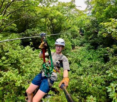 Ein junger Erwachsener, der an einem Zipline-Hochseil durch üppiges, grünes Blattwerk schwingt.