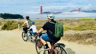 Eine Familie fährt mit Fahrrädern auf einem Weg, während die Golden Gate Bridge im Hintergrund sichtbar ist.