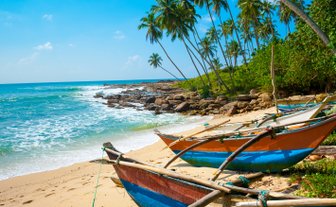 Sandstrand mit Booten neben dem klaren Wasser und Palmen im Hintergrund – Sri Lanka mit Kindern