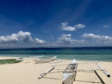 Ein ruhiger Strand mit sanftem, klarem Wasser und weißen Booten, die am Ufer auf weichem Sand liegen.