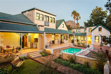 Ein elegantes, zweigeschossiges Haus mit grünem Dach, umgeben von einem gepflegten Garten und einem einladenden Pool.