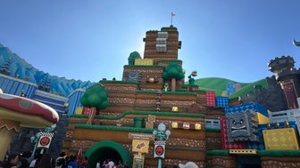 Ein lebhaftes Freizeitpark-Szenario mit einer bunten Mario Kart Attraktion und vielen Besuchern, die sich versammeln.