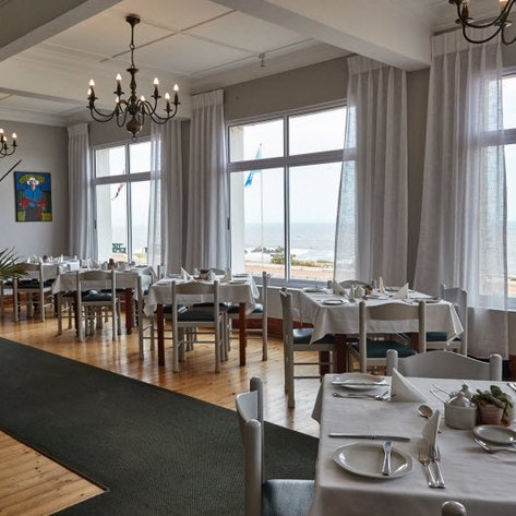 Ein eleganter Restaurantbereich mit weißen Tischen und Blick auf das Meer, umgeben von großen Fenstern und sanften Vorhängen.