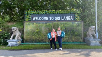 Zwei Frauen machen ein Erinnerungsfoto vor dem „Welcome to Sri Lanka“-Schriftzug am Flughafen – Sri Lanka Reise mit Kindern