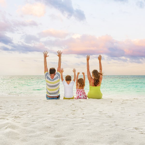Eine Familie sitzt am Strand und hebt die Hände in die Luft, während sie den Sonnenuntergang über dem Meer genießen.