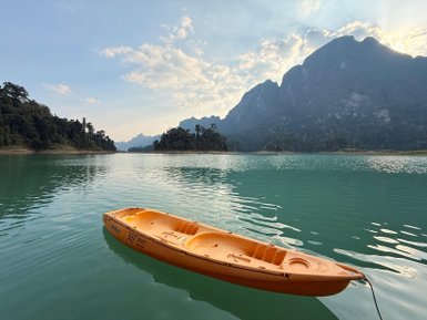 Ein leuchtend orangefarbenes Kajak schwimmt ruhig auf dem glitzernden Wasser eines ruhigen Sees, umgeben von Bergen.
