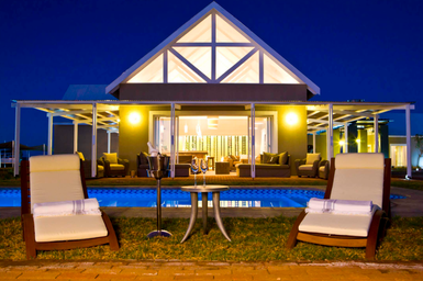 Eine Safari Lodge bei Nacht mit Pool im Vordergrund, Liegestühlen und beleuchtetem Gebäude im Hintergrund - Namibia Familienreise