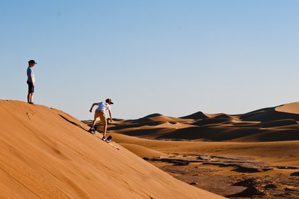 Kinder sausen mit Sandboards die hohen Dünen der Wüste hinunter – Marokko Familienreise