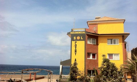 Ein farbenfrohes Gebäude mit der Aufschrift 'Residencial Sol Point' steht am Strand, umgeben von Pflanzen und Meer.