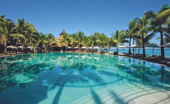 Ein glitzernder Pool spiegelt die Palmen und den strahlend blauen Himmel wider, umgeben von einem tropischen Paradies.