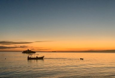 Ein ruhiger Sonnenuntergang über dem Meer, mit sanften Wellen und einem Boot, das langsam in der Ferne fährt.