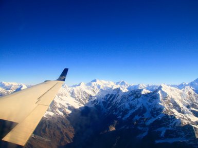 Der Blick aus dem Flugzeug zeigt majestätische schneebedeckte Berge unter einem klaren blauen Himmel.