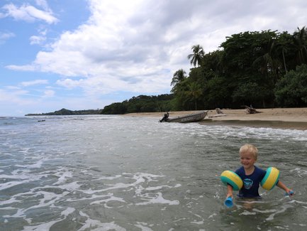 Kleines Kind planscht fröhlich im seichten Wasser am Strand – Costa Rica Reise mit Kindern