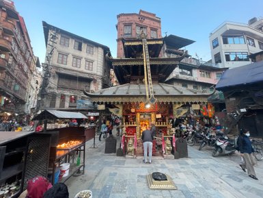 Ein geschäftiger Platz in Kathmandu mit einem prächtigen Tempel, umgeben von historischen Gebäuden und Menschen, die beten.