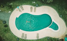 Ein Schwimmer entspannt in einem ausladenden Pool, umgeben von Sonnenliegen und üppiger Pflanzenwelt.