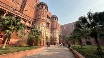 Das Rote Fort in Agra zeigt beeindruckende rote Sandsteinarchitektur, umgeben von üppigen Palmen und einem klaren Himmel.