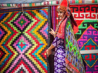 Eine einheimische Frau in traditioneller Kleidung öffnet einen bunten Vorhang aus kunstvollen Textilien.