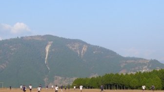 Eine Gruppe von Spielern läuft auf einem offenen Feld, umgeben von Bergen und Bäumen, während sie ein Fußballspiel spielen.